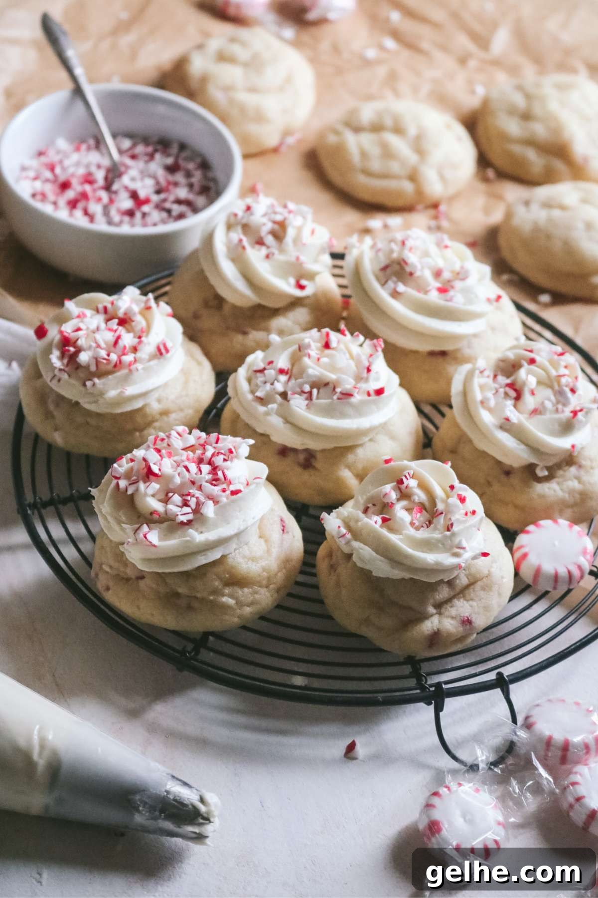 frosted peppermint sugar cookies on a wire rack with extra unfrosted cookies in the back and a bowl of crushed mint candies.