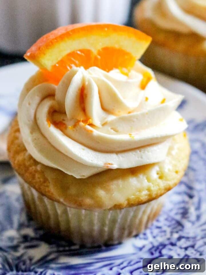 close up view of a fresh orange cupcake on a blue and white plate with orange buttercream and a sliced orange on top.