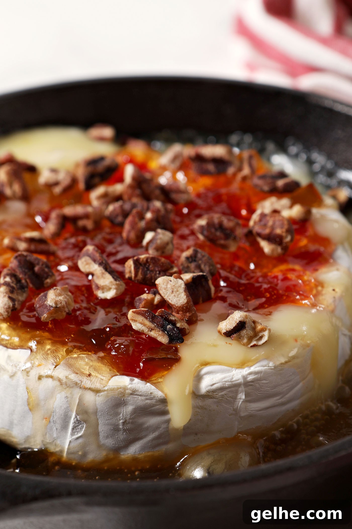 Close up of melty Baked Brie with Pepper Jelly and Toasted Pecans in a cast iron skillet