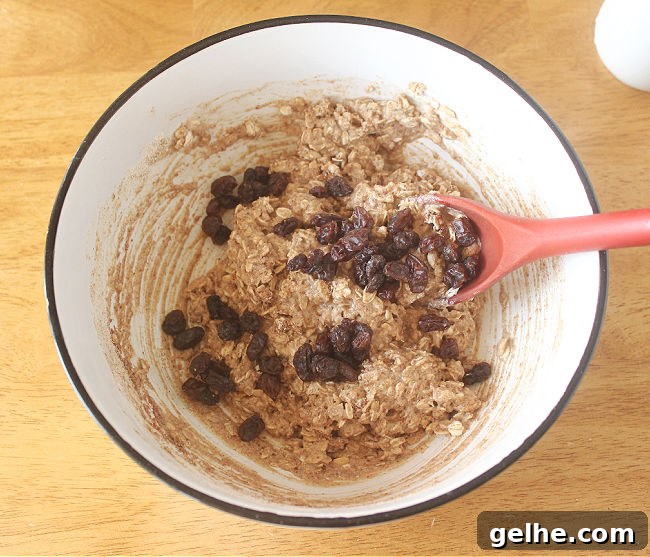 Cookie dough with raisins being stirred with a red spoon.