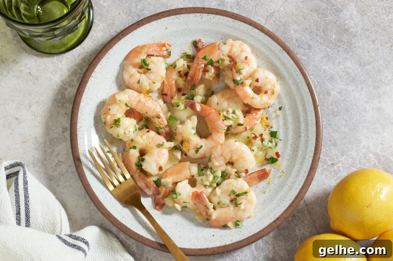Quick Shrimp Scampi with Lemony Garlic Sauce 9 Shrimp scampi on a plate with a gold fork. The plate is surrounded by a green glass, three lemons, and a blue and white striped napkin.