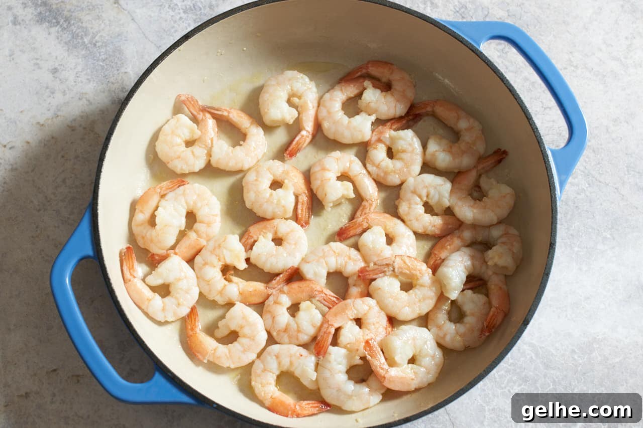 Quick Shrimp Scampi with Lemony Garlic Sauce 6 Shrimp cooking in a pan with blue handles.