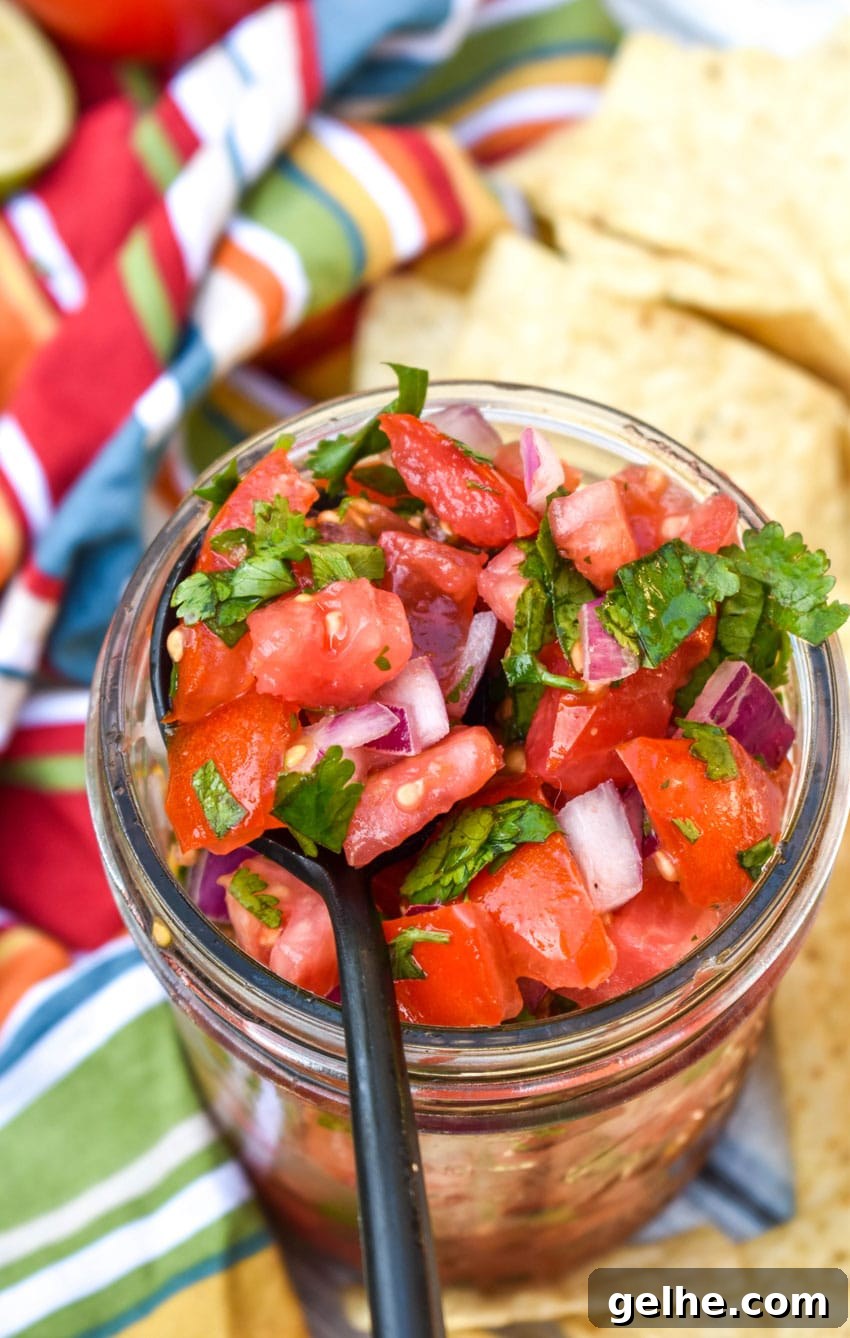 a black spoon scooping homemade pico de gallo from a small glass jar