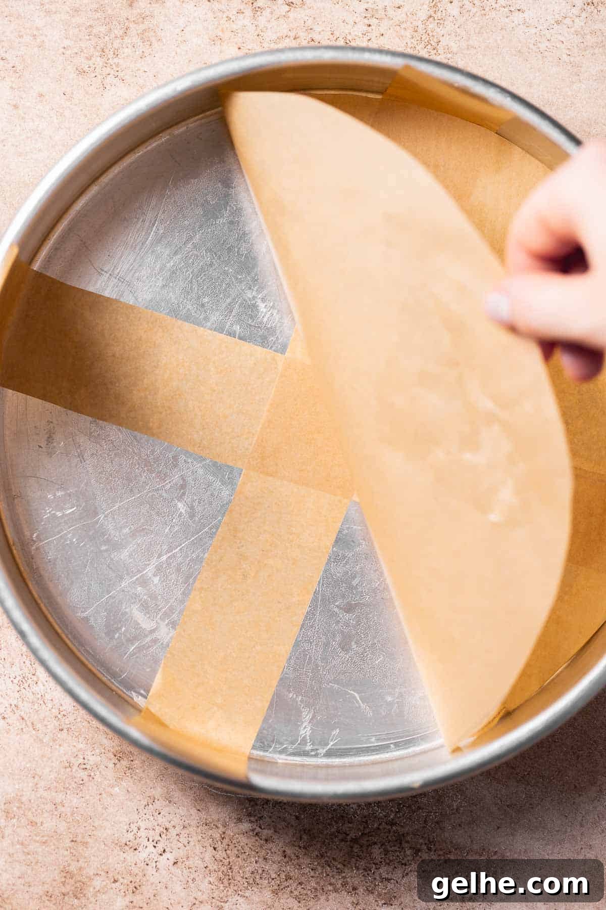 A round cake pan being lined with parchment paper.
