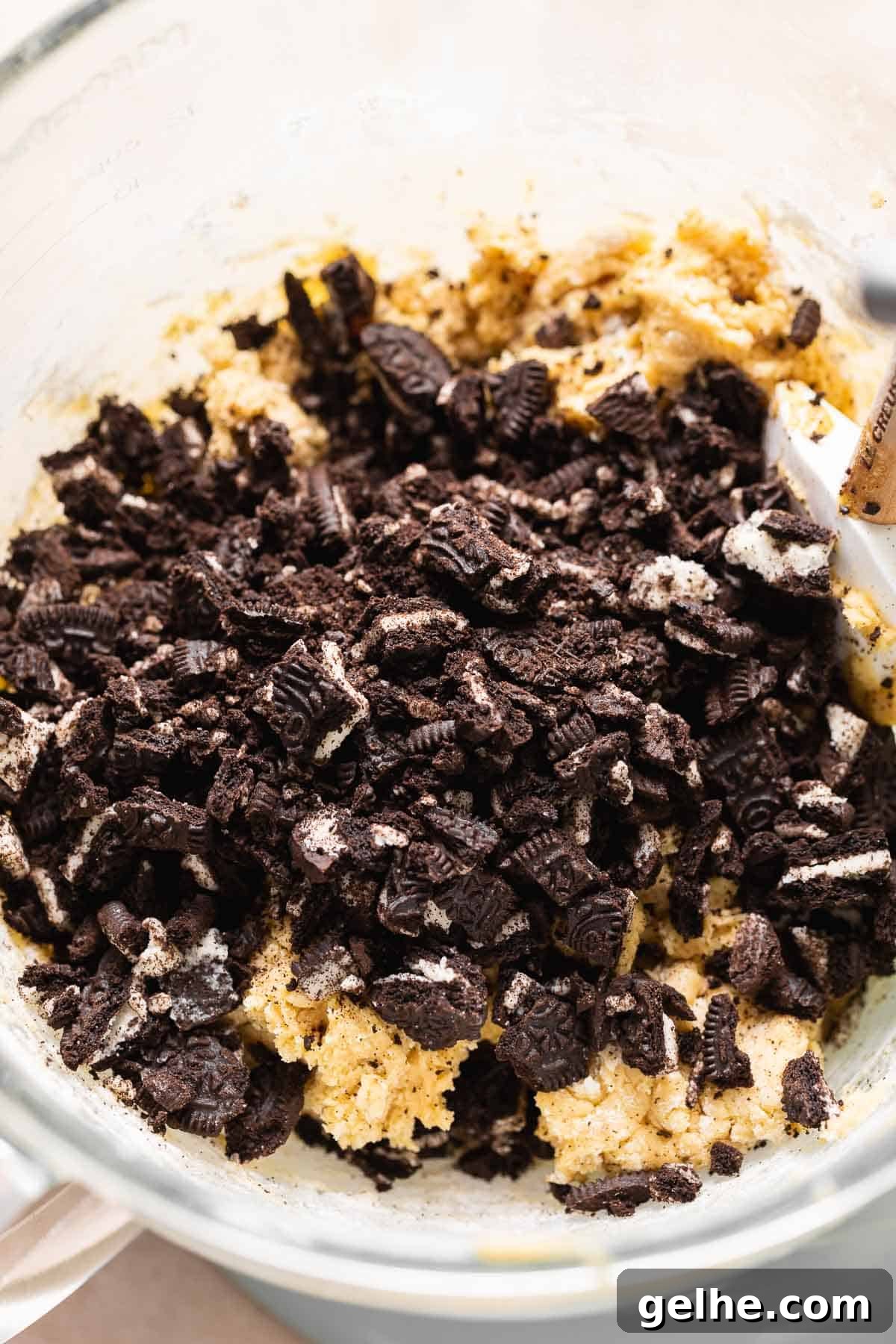 A mixing bowl with chopped oreo cookies on top of the cookie dough before mixing.