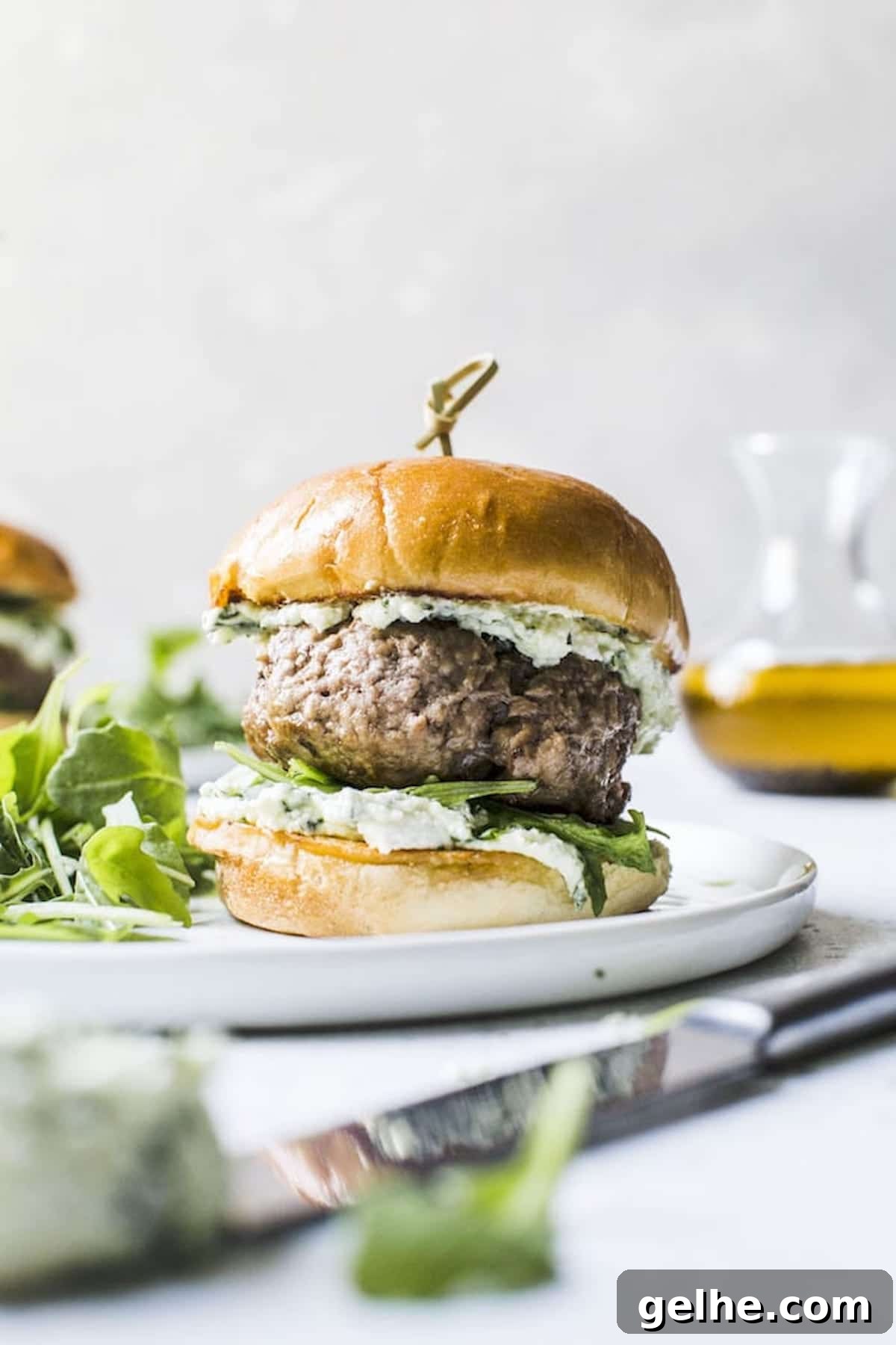 side view of a lamb burger assembled on a bun with pesto whipped feta on a plate.