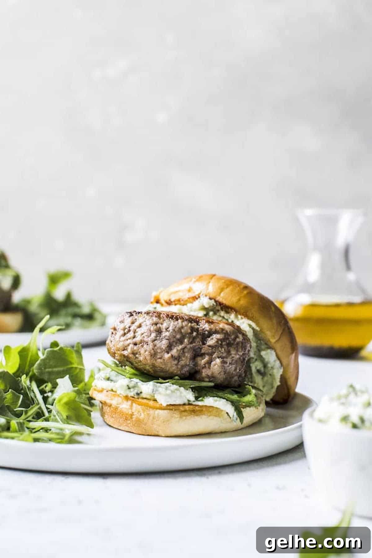 side view of a lamb burger assembled on a bun with pesto whipped feta on a plate.