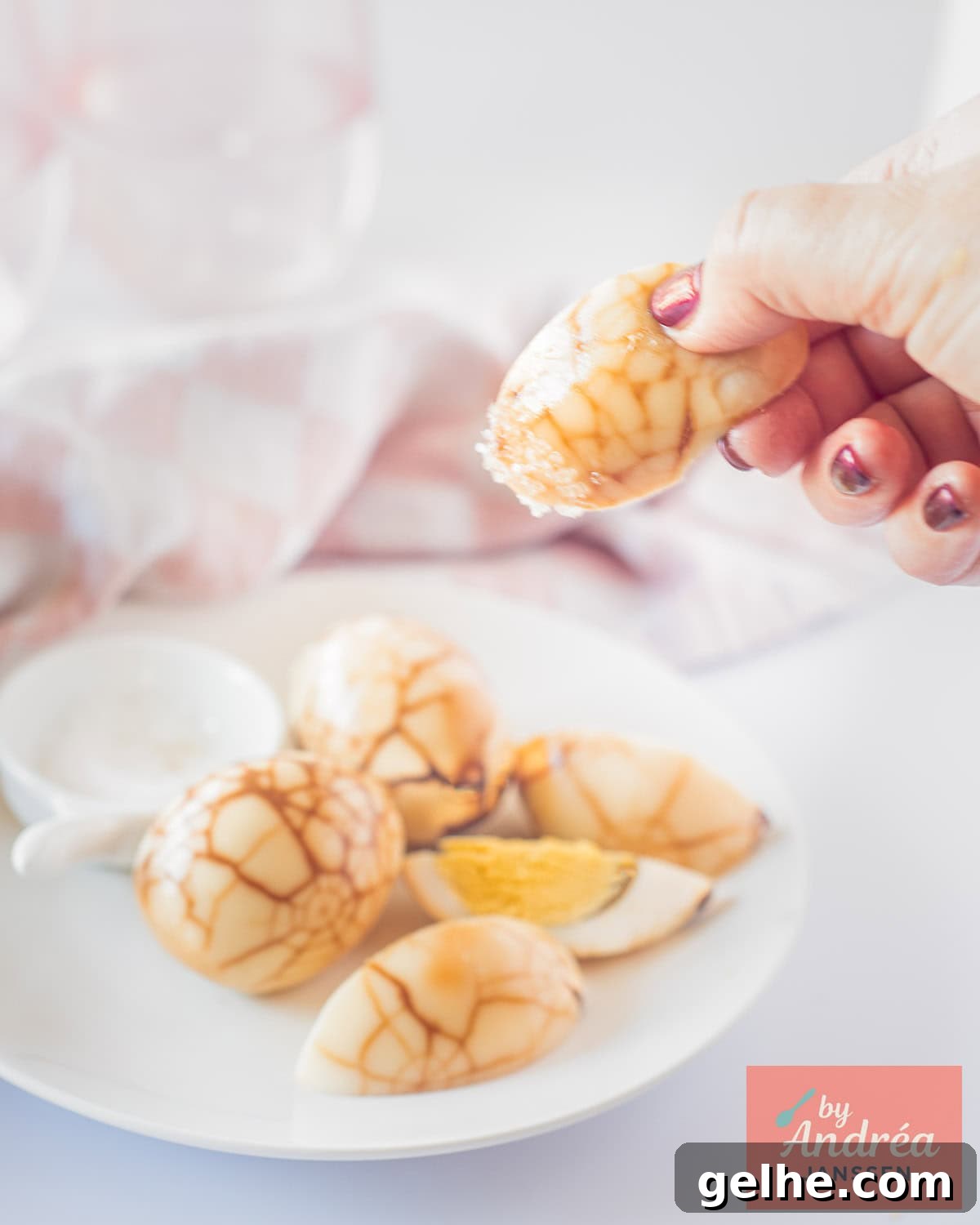 How to Make Chinese Tea Eggs: Savory Marble Egg Recipe 2 A white plate with tea eggs, a hand picking one dipped in salt.