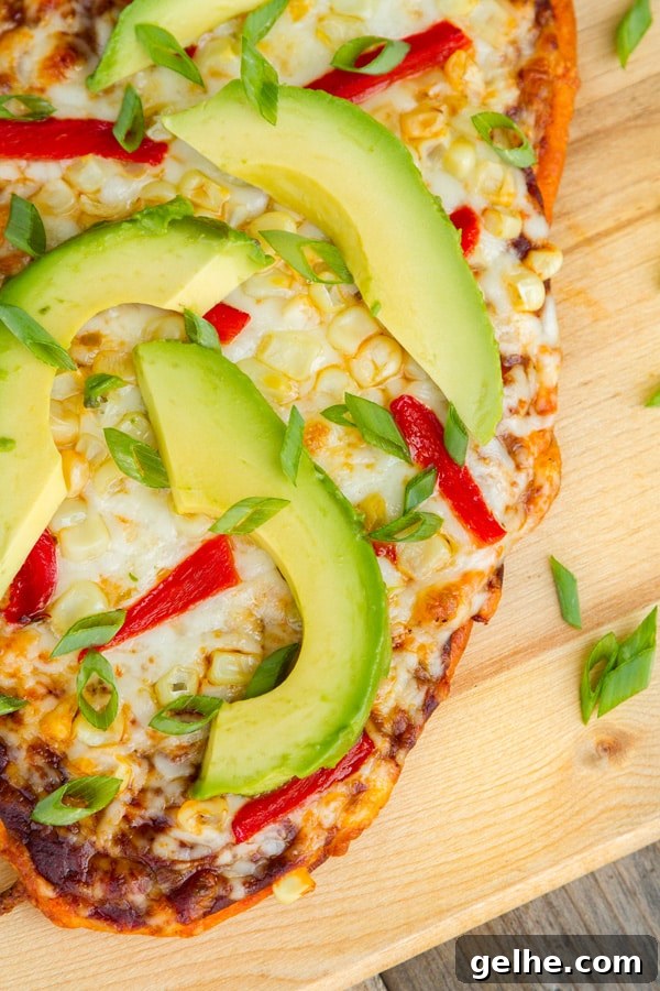 looking down on a pizza with cheese, red peppers, corn, and avocado.