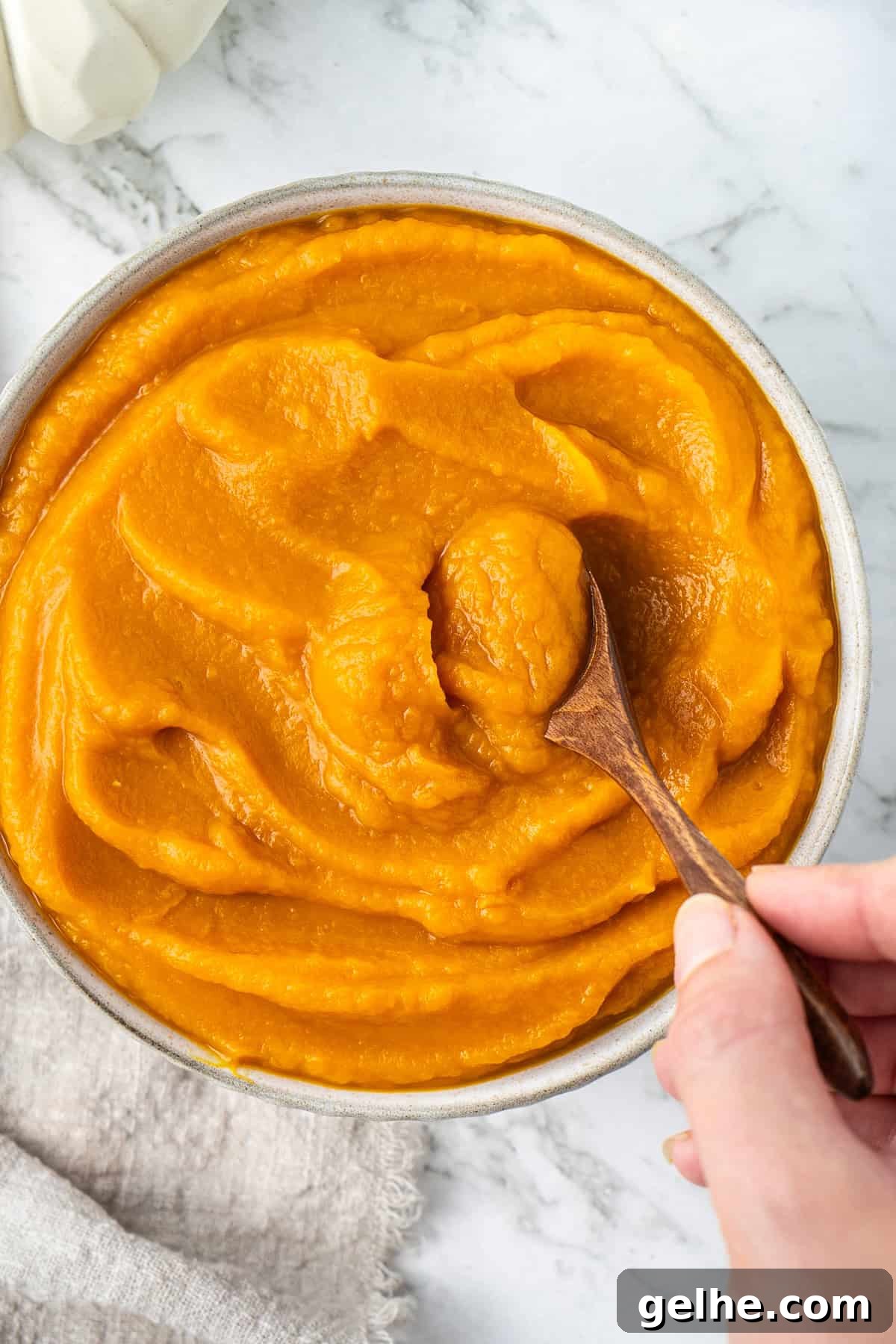 How to Make Smooth Homemade Pumpkin Puree for Baking 12 Close up of pumpkin puree in a bowl with a hand scooping some with a spoon.