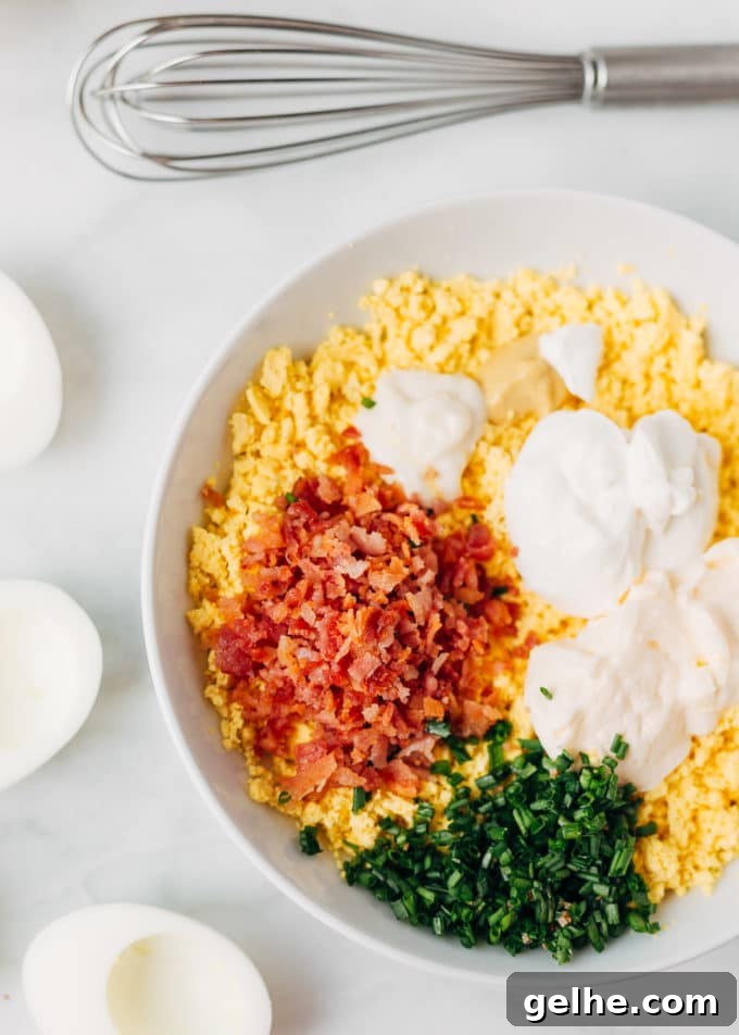 Bacon-Stuffed Deviled Eggs with Zesty Horseradish 3 crumbled egg yolks in a bowl with bacon, mayonnaise, sour cream, and chives