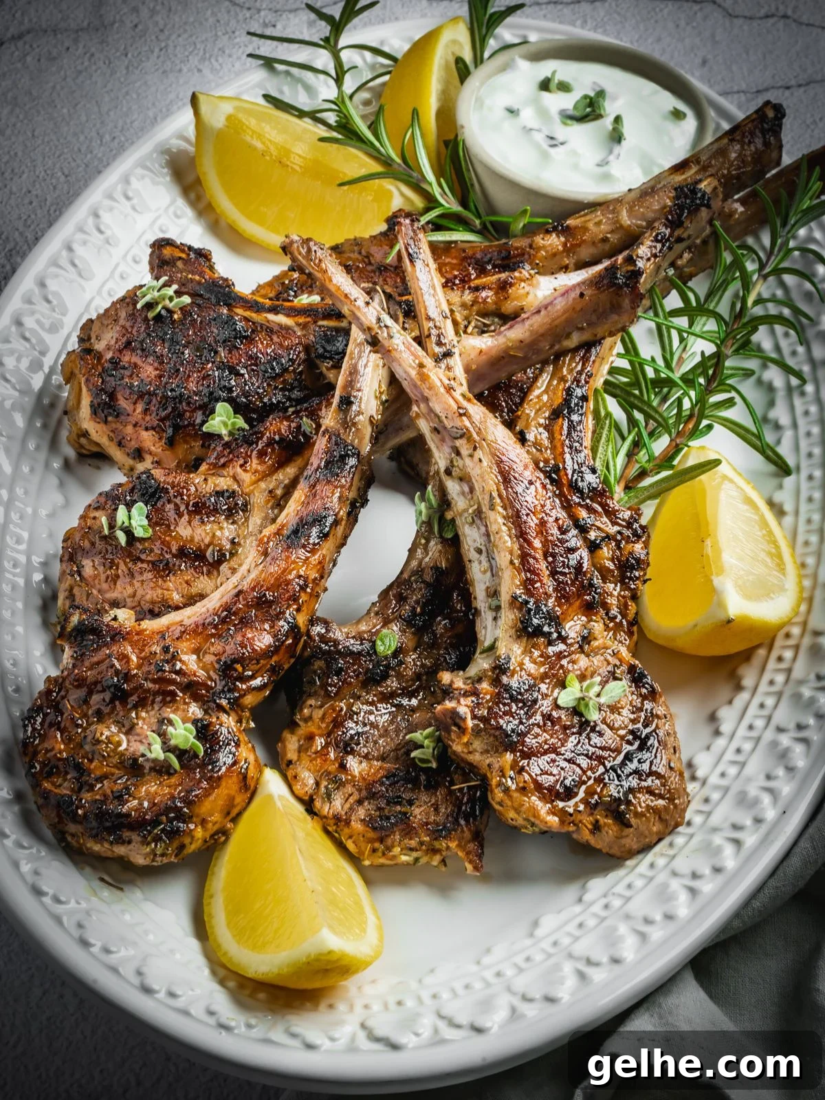 Grilled and marinated Greek lamb chops on a platter with rosemary and lemon wedges.
