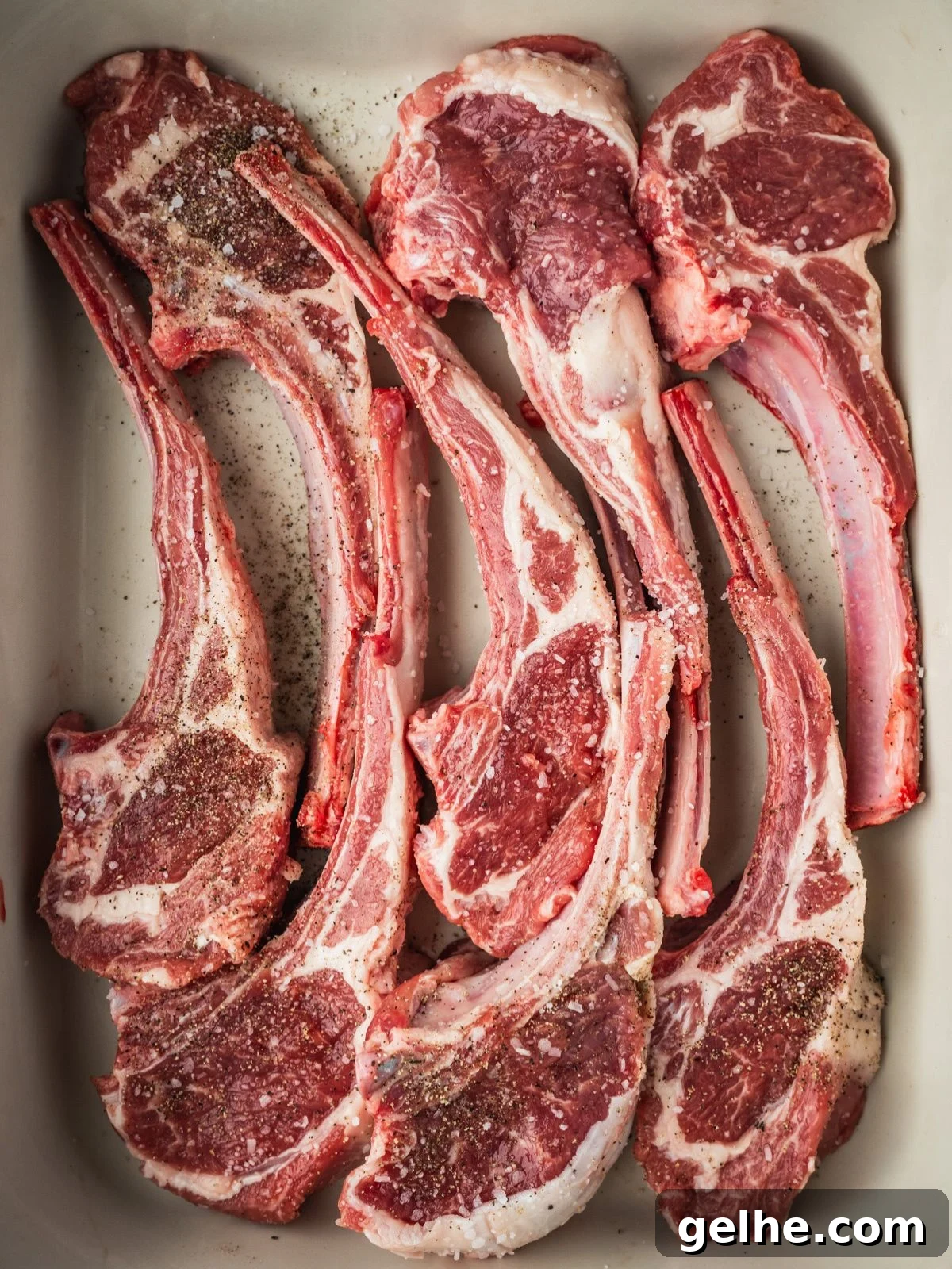 Lamb chops in a tray seasoned with salt and pepper.