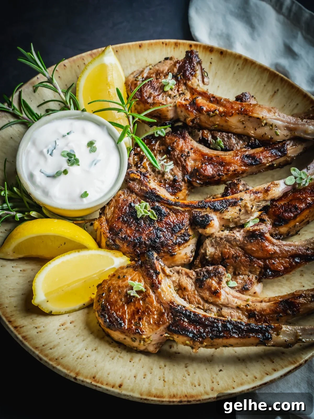 Grilled and marinated Greek lamb chops on a platter with rosemary and lemon wedges.