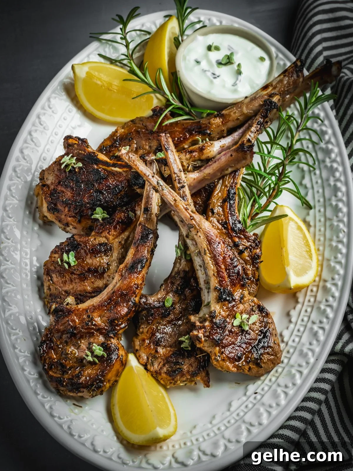 Grilled and marinated Greek lamb chops on a platter with rosemary and lemon wedges.