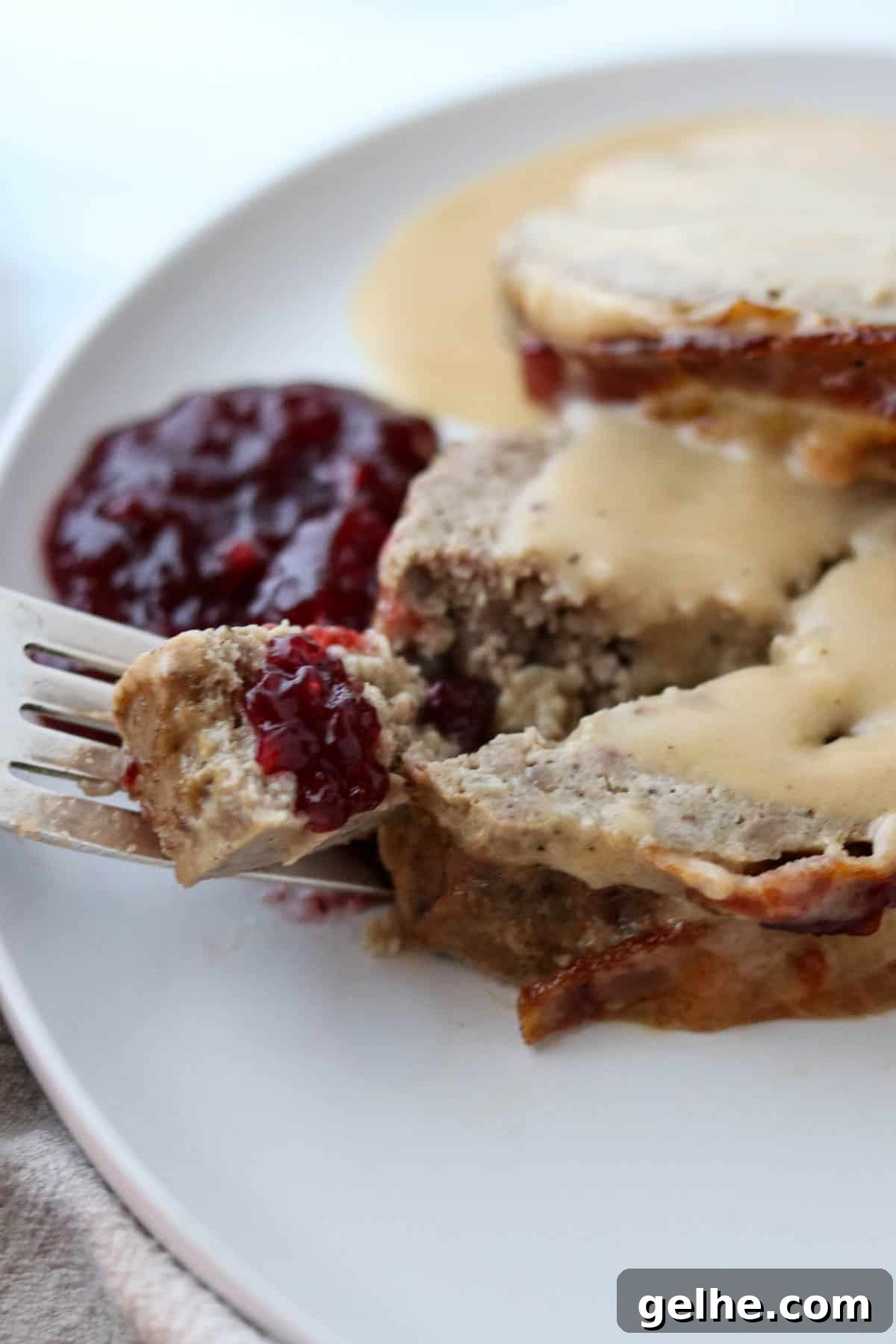 A bite of Danish Meatloaf on a fork with lingonberries.