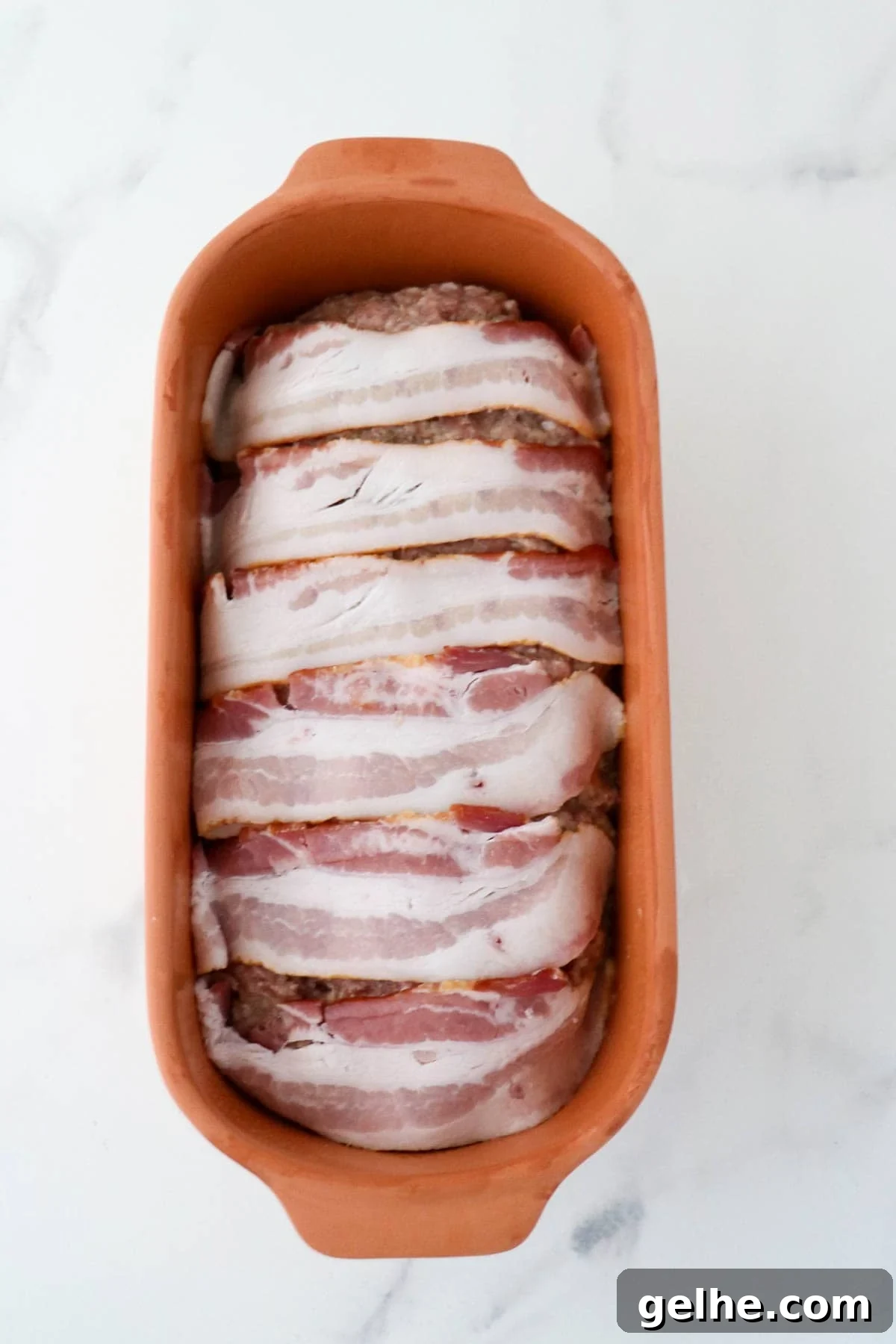 Danish meatloaf in a clay baker topped with bacon slices.