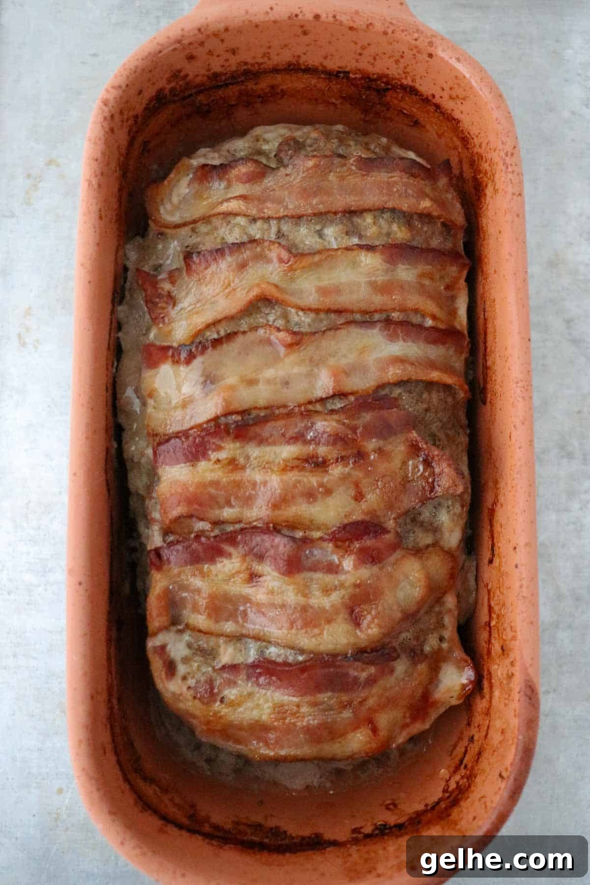 Baked Danish Meatloaf topped with bacon in a clay baker.