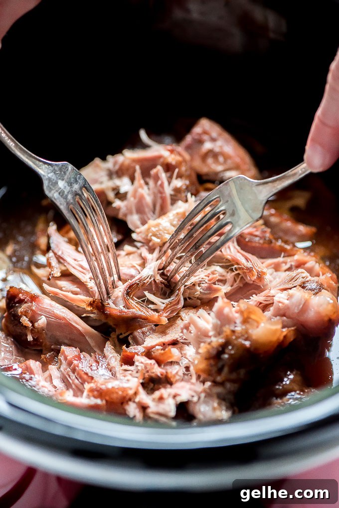 Shredding Slow Cooker Kalua Pork with two forks in a Crock-Pot.