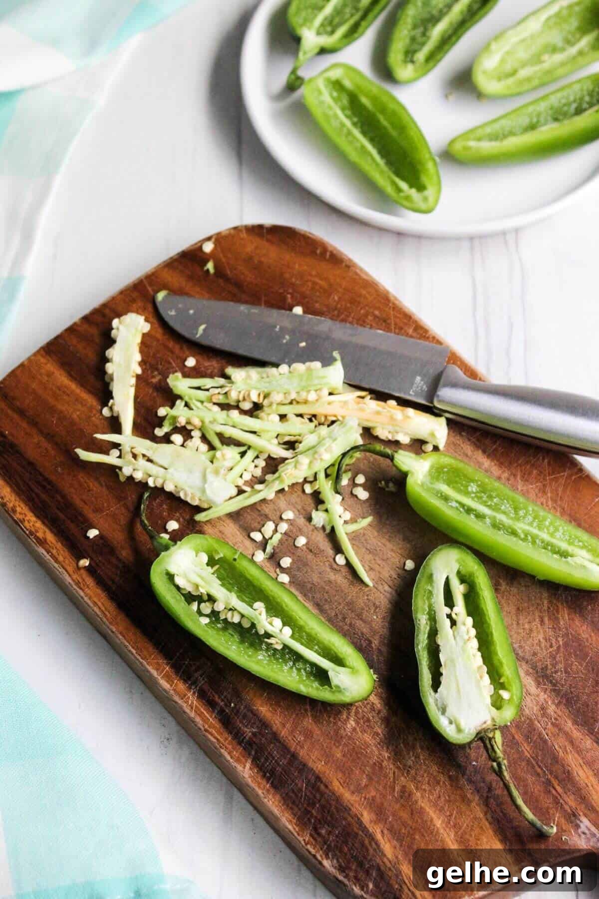 Jalapeño peppers cut in half on cutting board removing seeds.