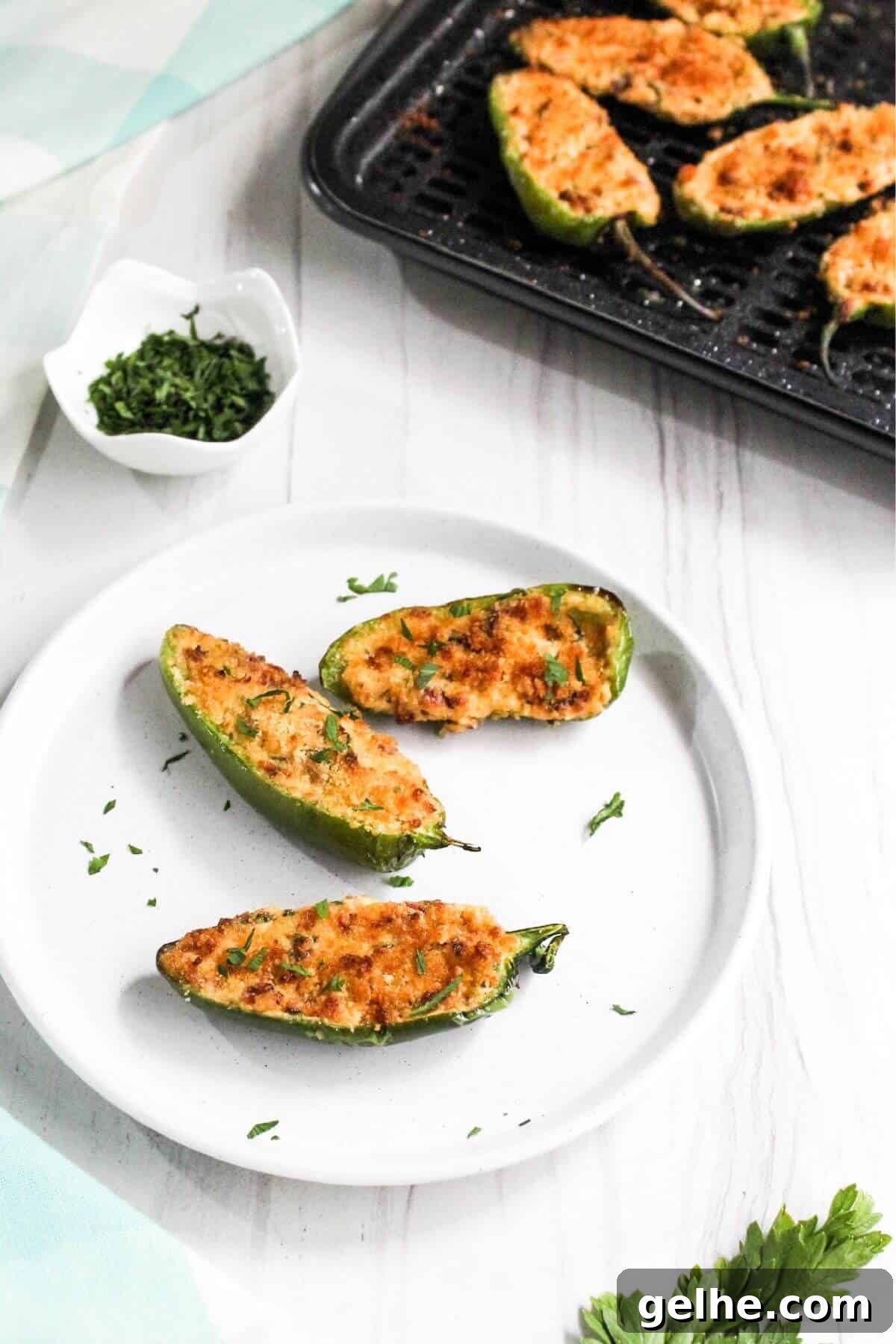 Three jalapeño poppers on white plate with air fryer tray in back.
