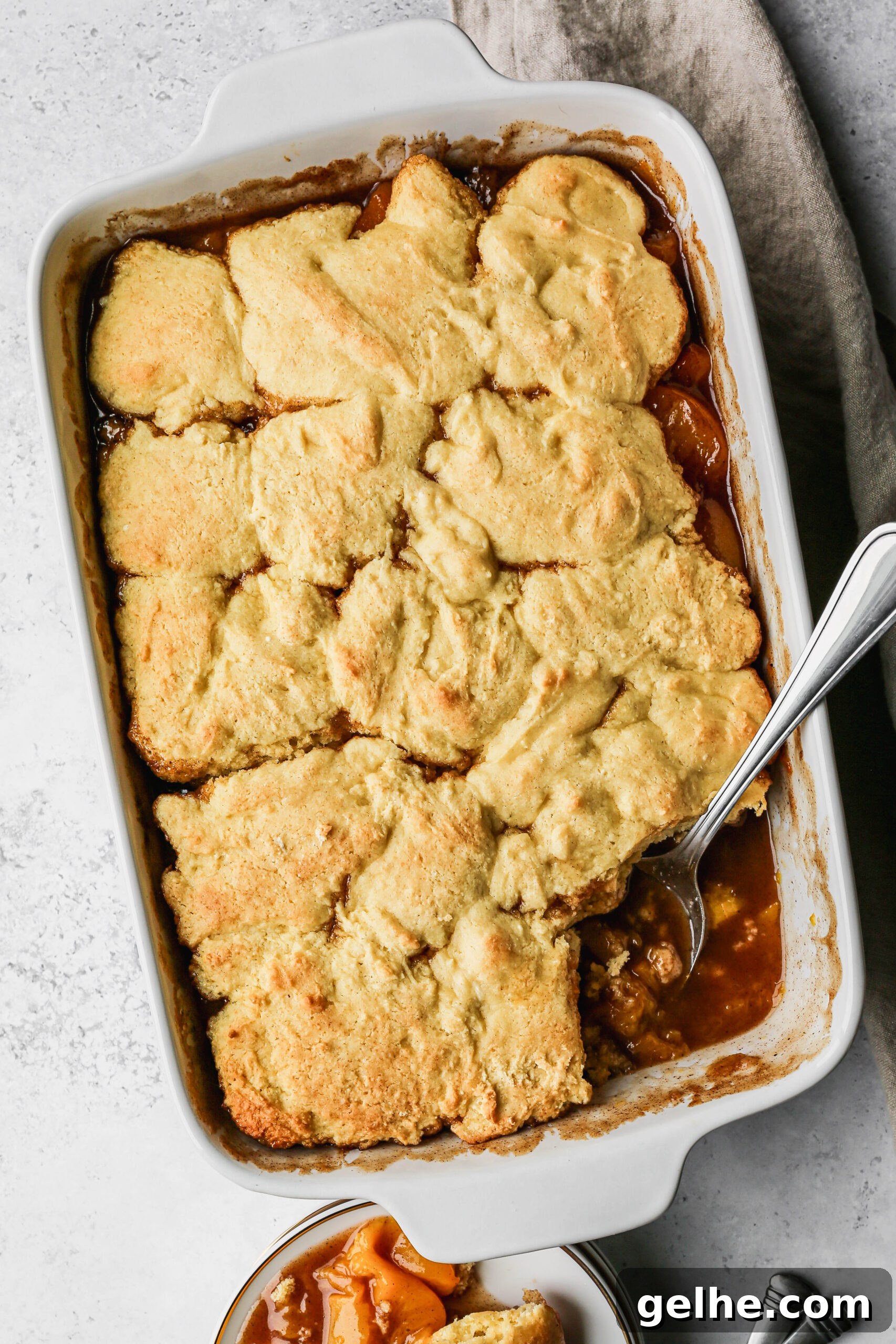 a white baking dish of gluten free canned peach cobbler next to a white plate of cobbler.