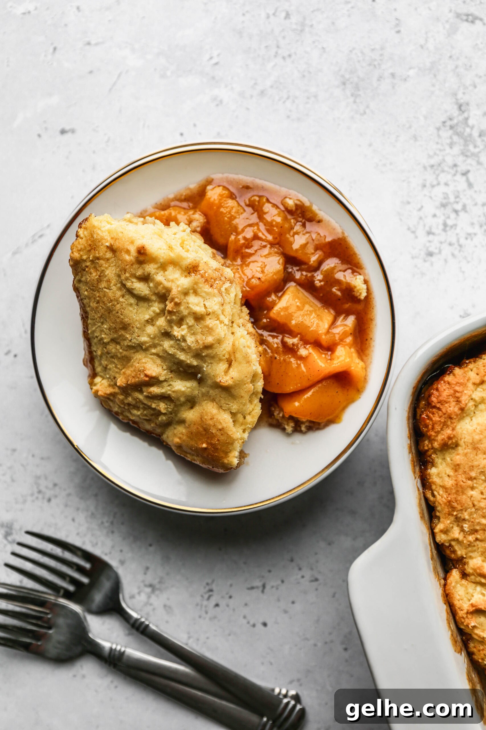 a white plate of gluten free canned peach cobbler next to a white baking dish of cobbler.