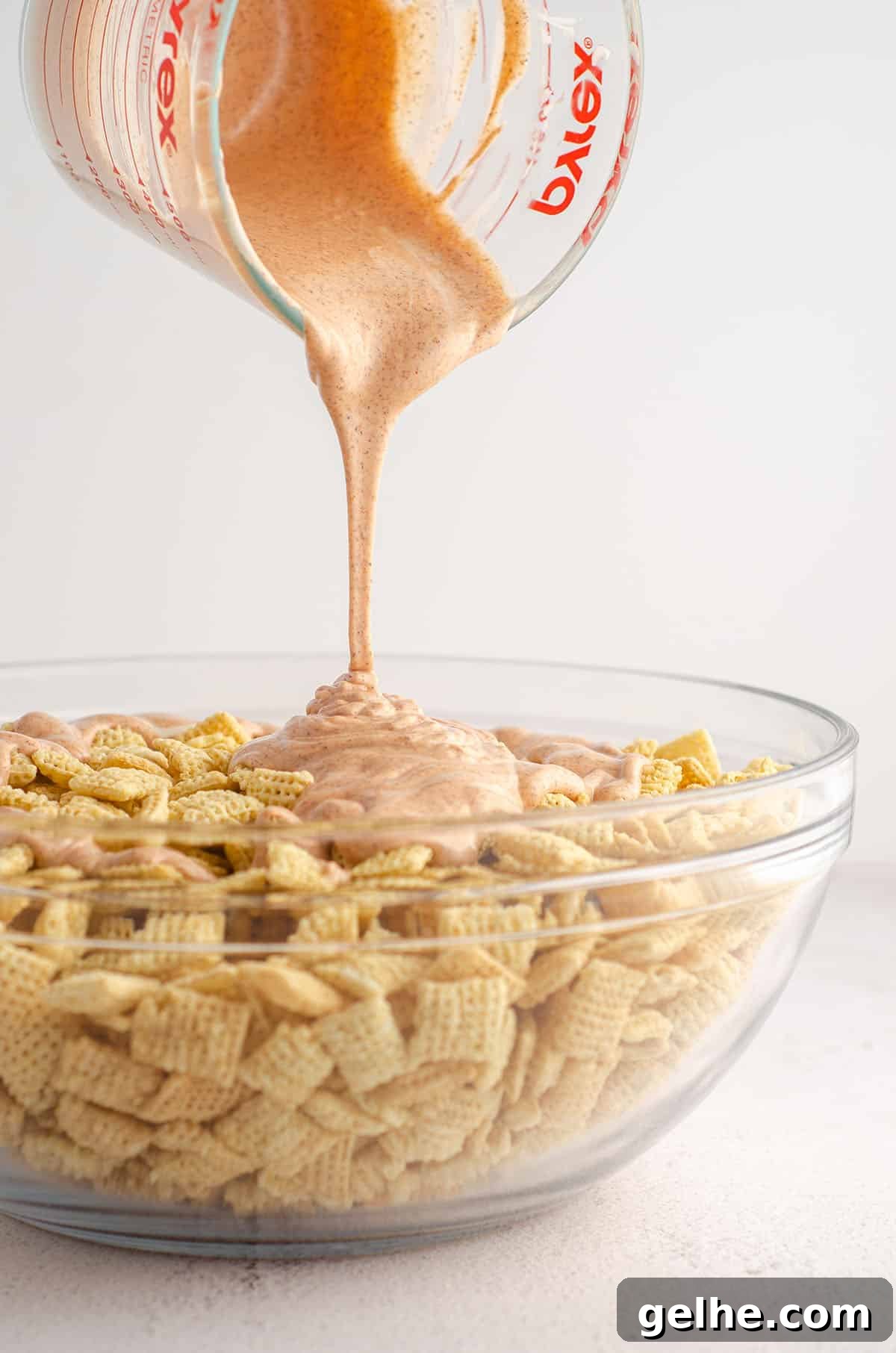chex sitting in a glass bowl and orange candy melts being poured over them for pumpkin spice puppy chow