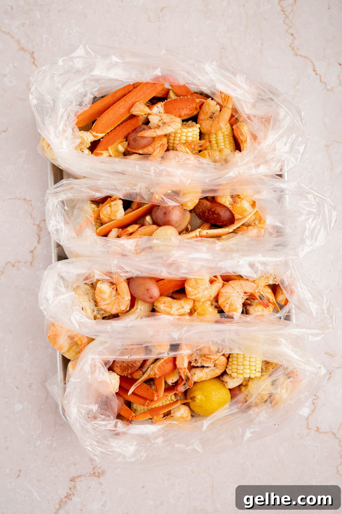 The drained seafood, corn, sausage, and potatoes divided into 4 bags on a white countertop.