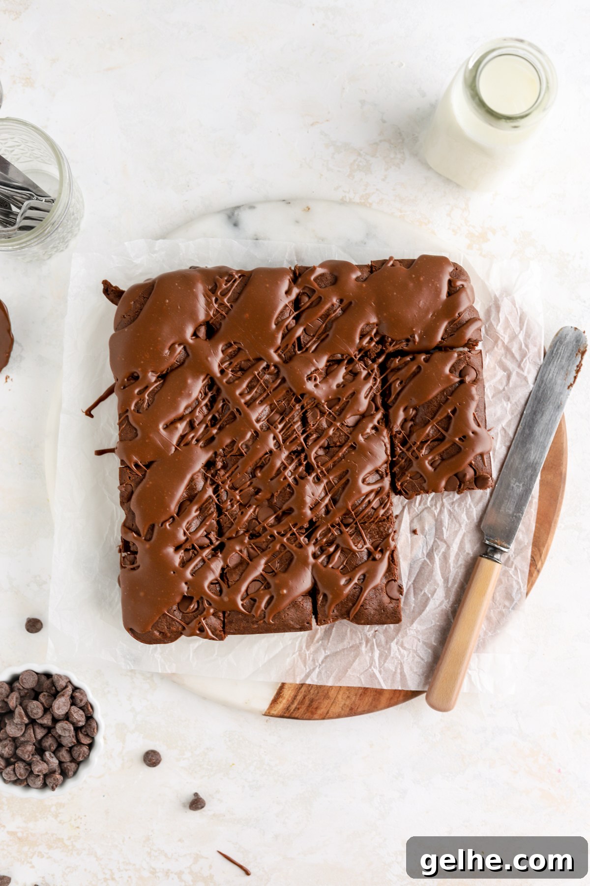 Fudgy Condensed Milk Brownies with a Creamy Caramel Swirl 3 Brownies drizzled with a knife and bowl of chocolate chips next to them.