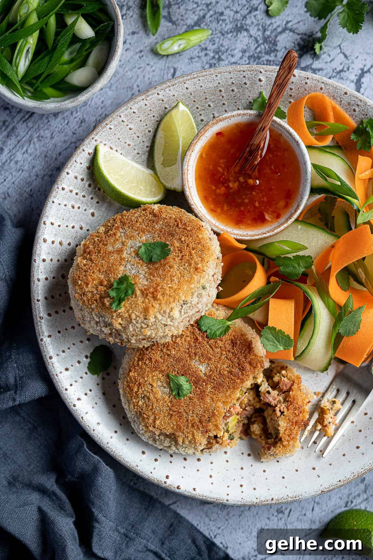 Close up of two vegan fish cakes on a white plate with vegetable ribbons and sweet chilli sauce.