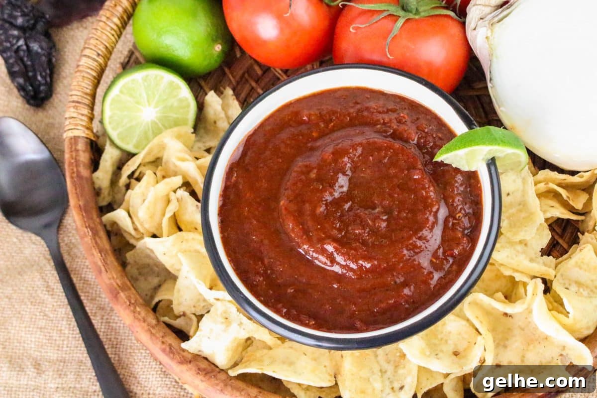 Authentic Red Salsa Roja with Dried Chiles Recipe 2 Top down view of a basket filled with tortilla chips with a bowl of rojo salsa sitting in the center. - Hostess At Heart