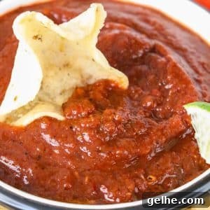 Authentic Red Salsa Roja with Dried Chiles Recipe 11 A bowl of deep read rojo salsa with a tortilla chip dipped into the side. - Hostess At Heart