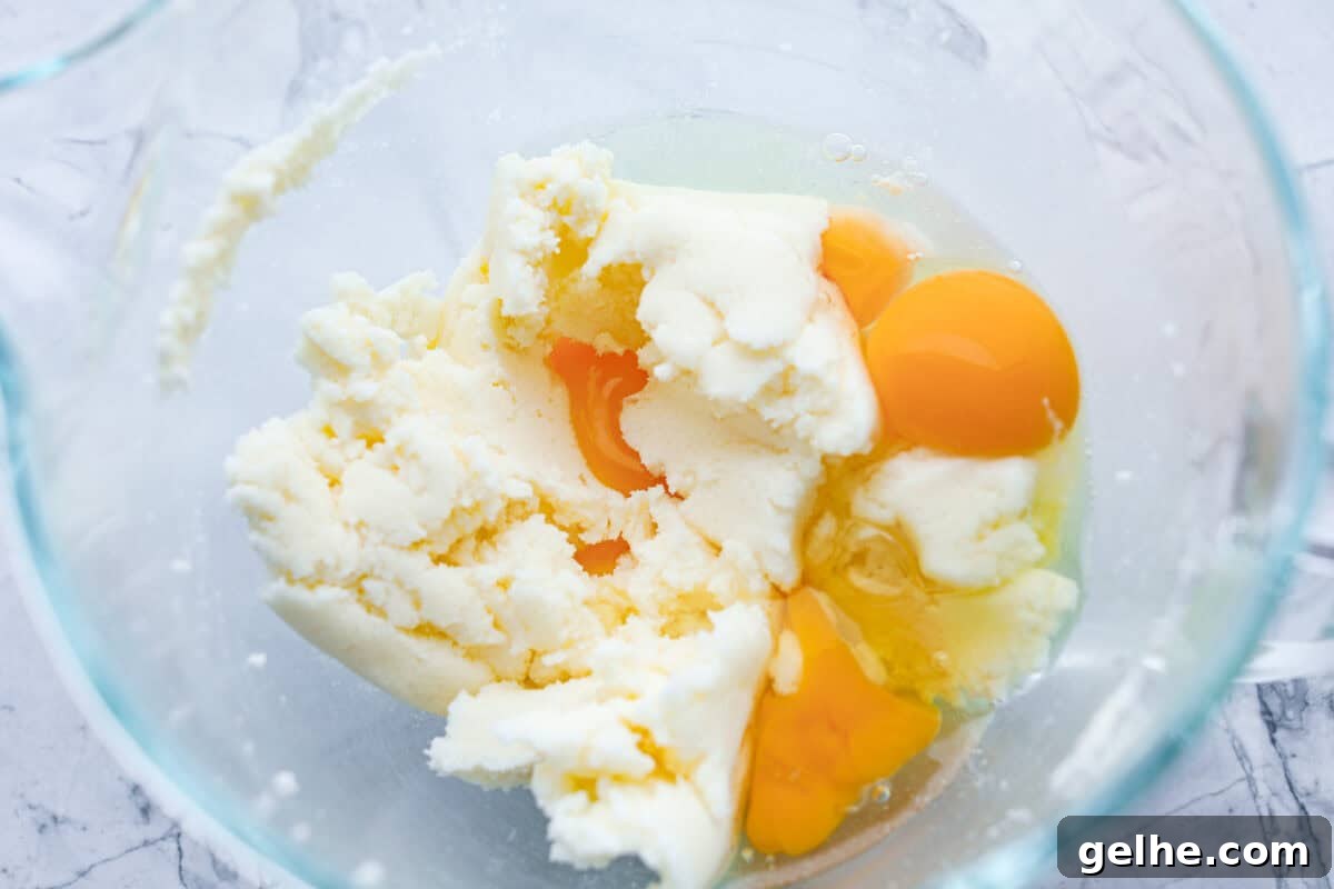 Eggs being beaten in a glass bowl with the sugar and butter mixture.