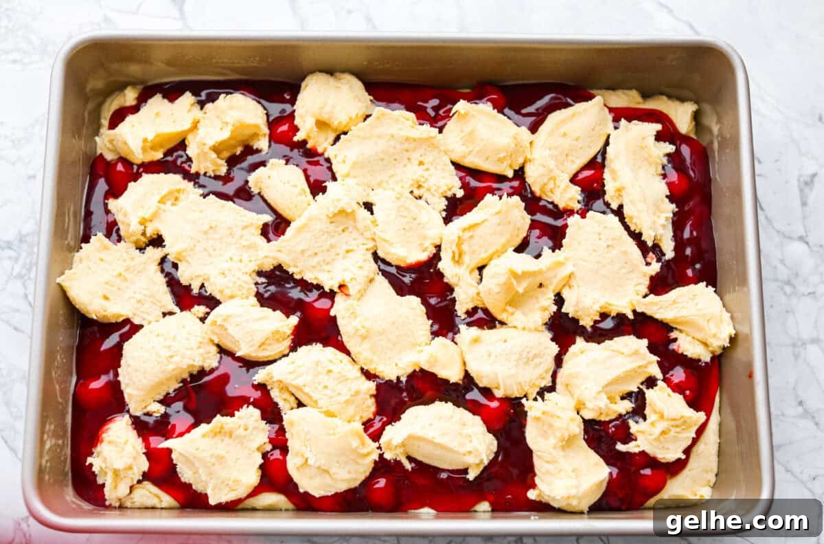 Remaining batter being spooned on top of the pie filling just before baking the cherry pie bars.