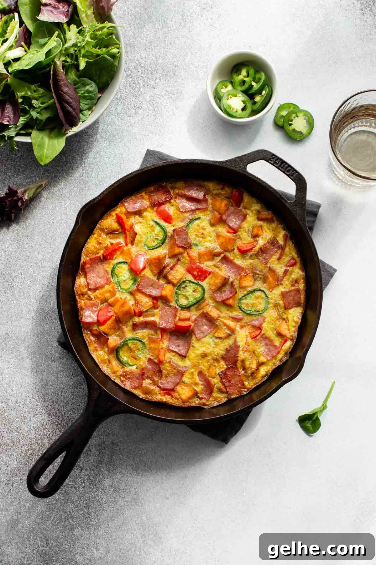 Overhead view of a sweet potato frittata in a cast iron skillet with a green salad off to the side.