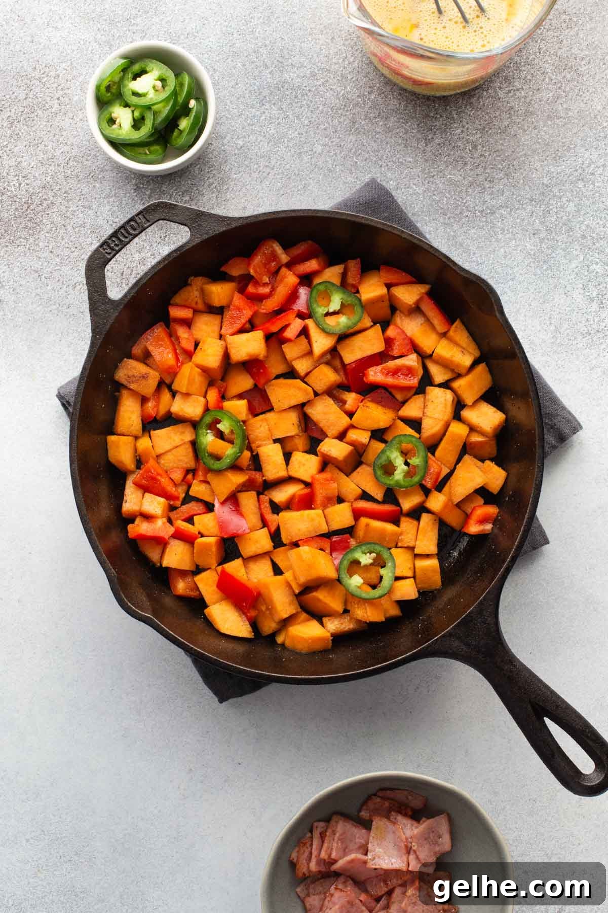 Sweet potatoes and peppers chopped and arranged in a cast iron skillet.