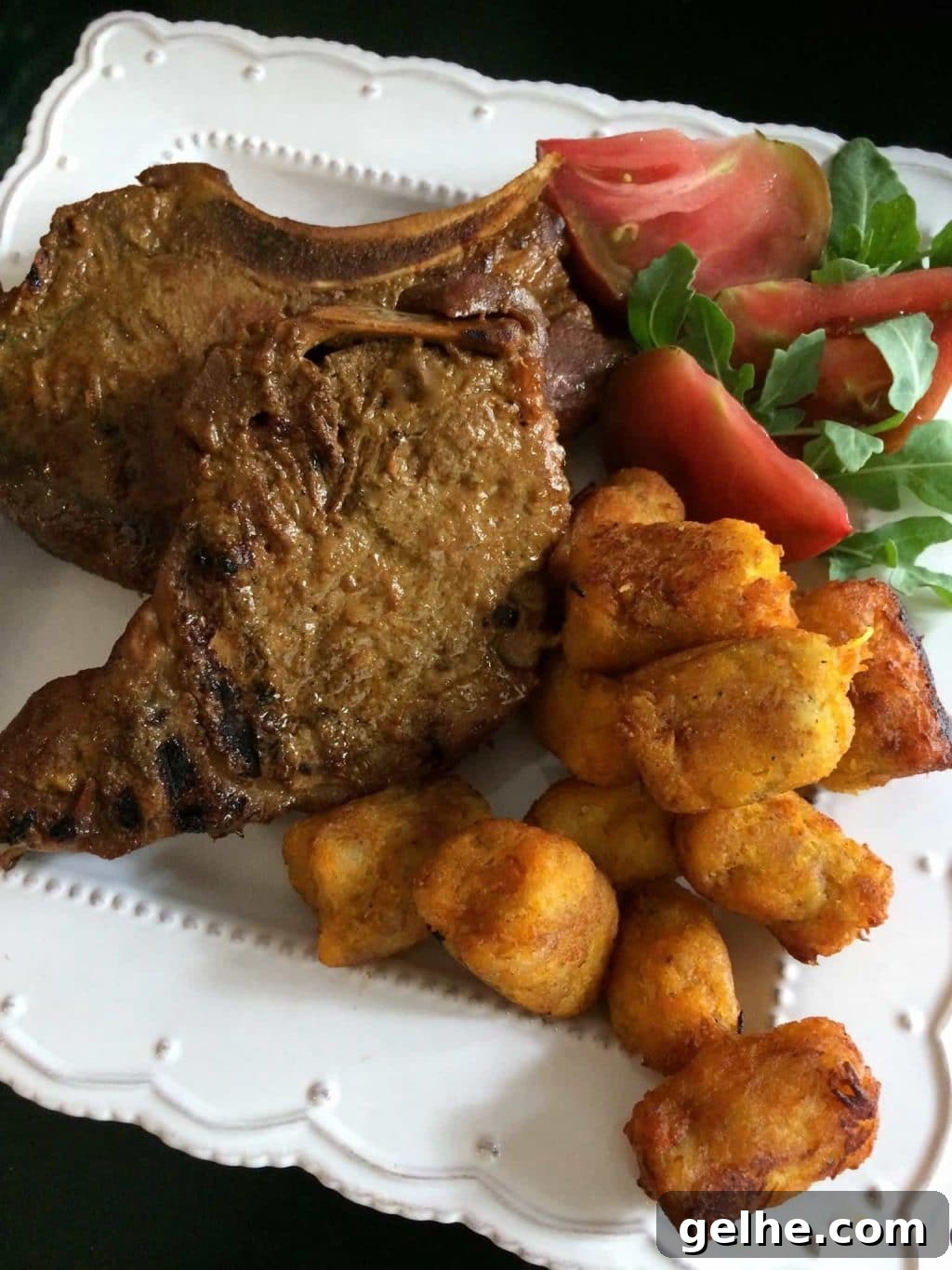 Molasses and mustard marinated pork chops from Heidi Billotto Food on a white platter with vegetable and tater tot garnish.