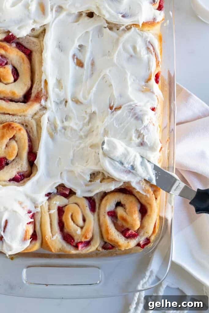 pan of strawberry rolls being frosted with cream cheese frosting