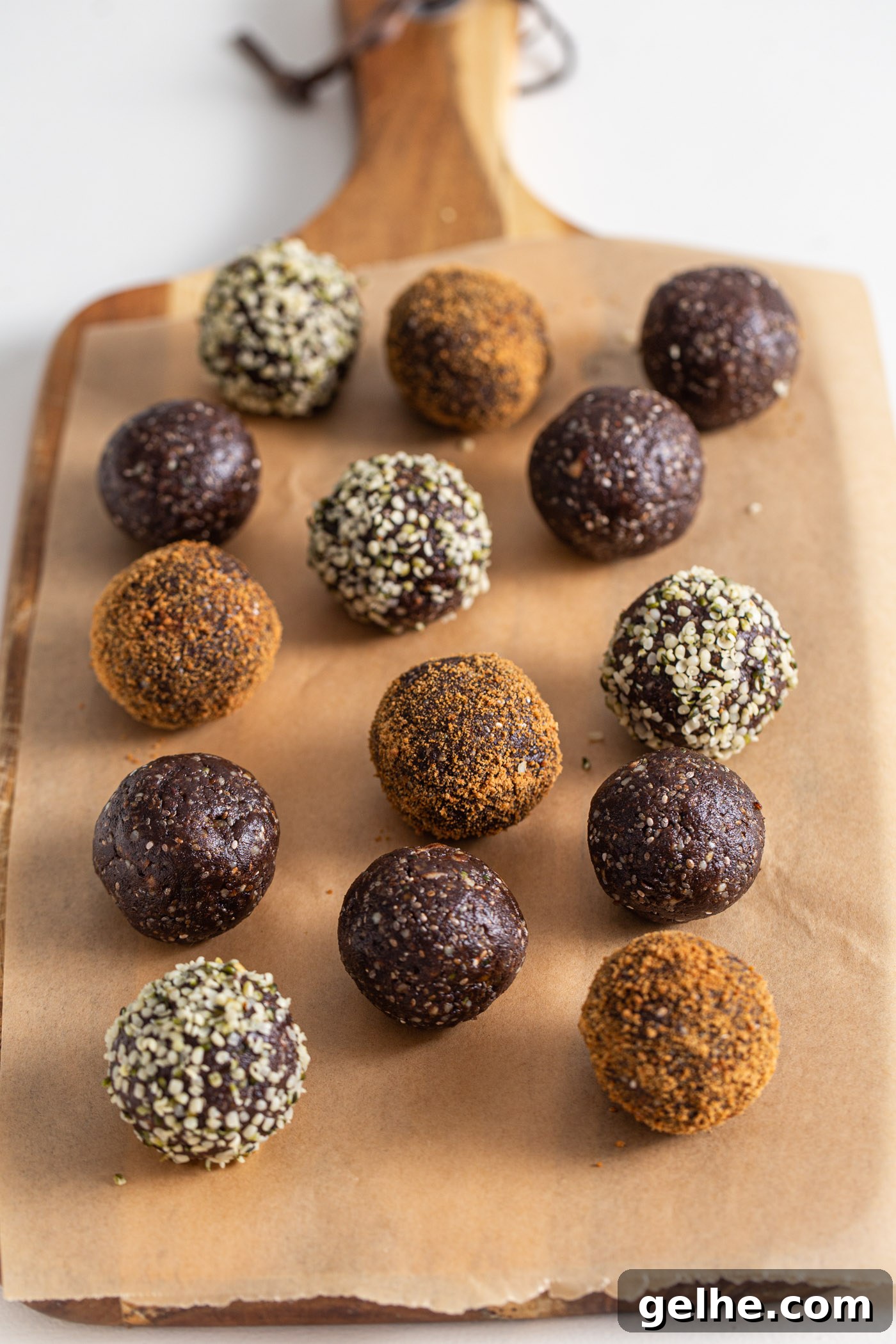 Chocolate energy balls rolled in coconut sugar and hemp seeds on a cutting board lined with parchment paper. The balls are made from dates, walnuts, cocoa and chia seeds.