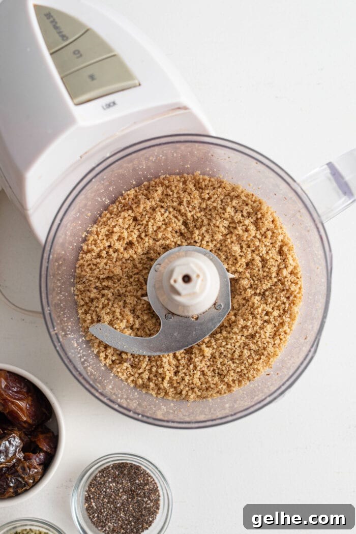Blended walnuts in a food processor. A small glass bowl of chia seeds and dates is beside the food processor.