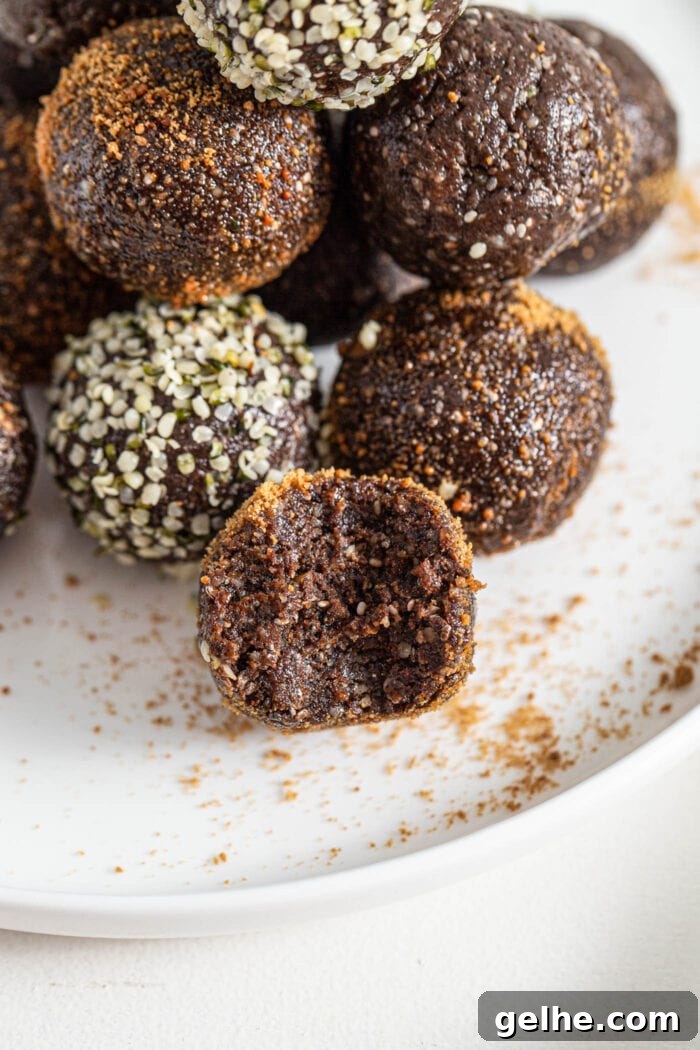 Close up of a superfood chocolate energy ball coated in coconut sugar with a bite taken out of it on a plate. There are more chocolate energy balls on plate in background, some are coated in hemp seeds.