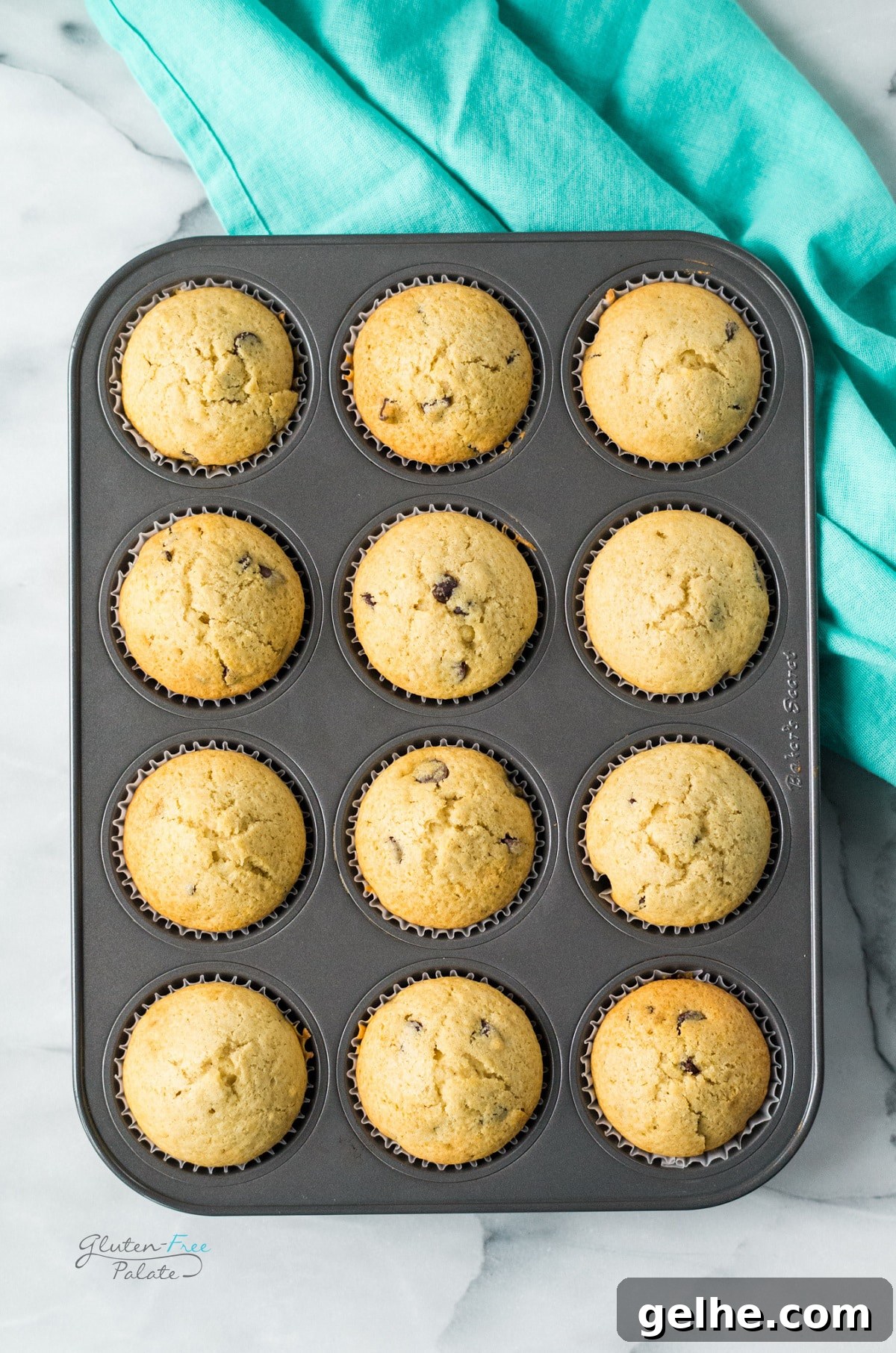 View from above of 12 gluten-free chocolate chip muffins in a muffin pan. a teal towel is underneath the pan.