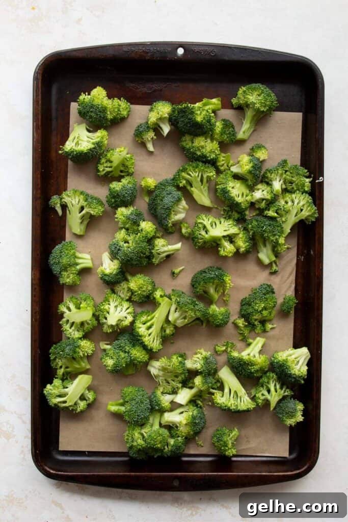 broccoli florets tossing in olive oil on a baking sheet before roasting in oven