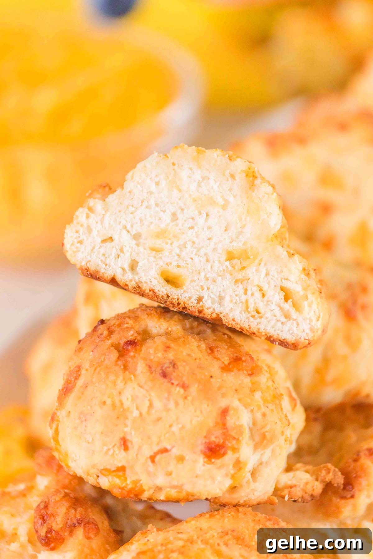 Flaky Cheddar Biscuits Made with Bisquick 12 A sliced Bisquick cheddar biscuit is placed on top of a stack of similar biscuits, showcasing its fluffy texture and bits of savory cheese.