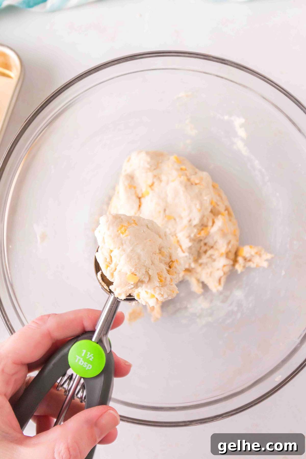 Flaky Cheddar Biscuits Made with Bisquick 15 A hand holds a 1.5-tablespoon scoop with dough, poised over a glass bowl brimming with more Bisquick cheddar biscuit dough.