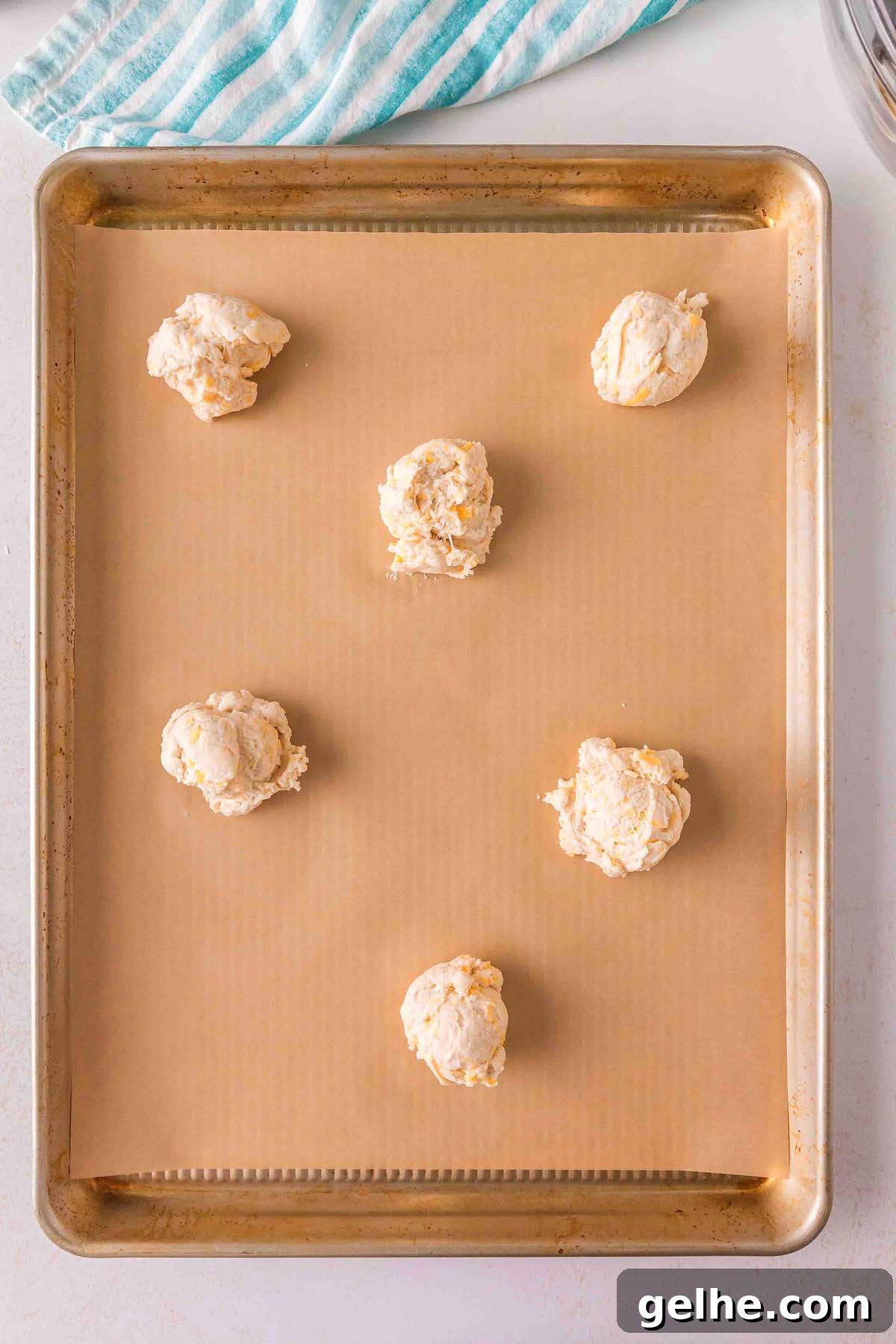 Flaky Cheddar Biscuits Made with Bisquick 16 Six scoops of dough, reminiscent of scrumptious Bisquick cheddar biscuits, are spaced evenly on a parchment-lined baking sheet, ready for baking.