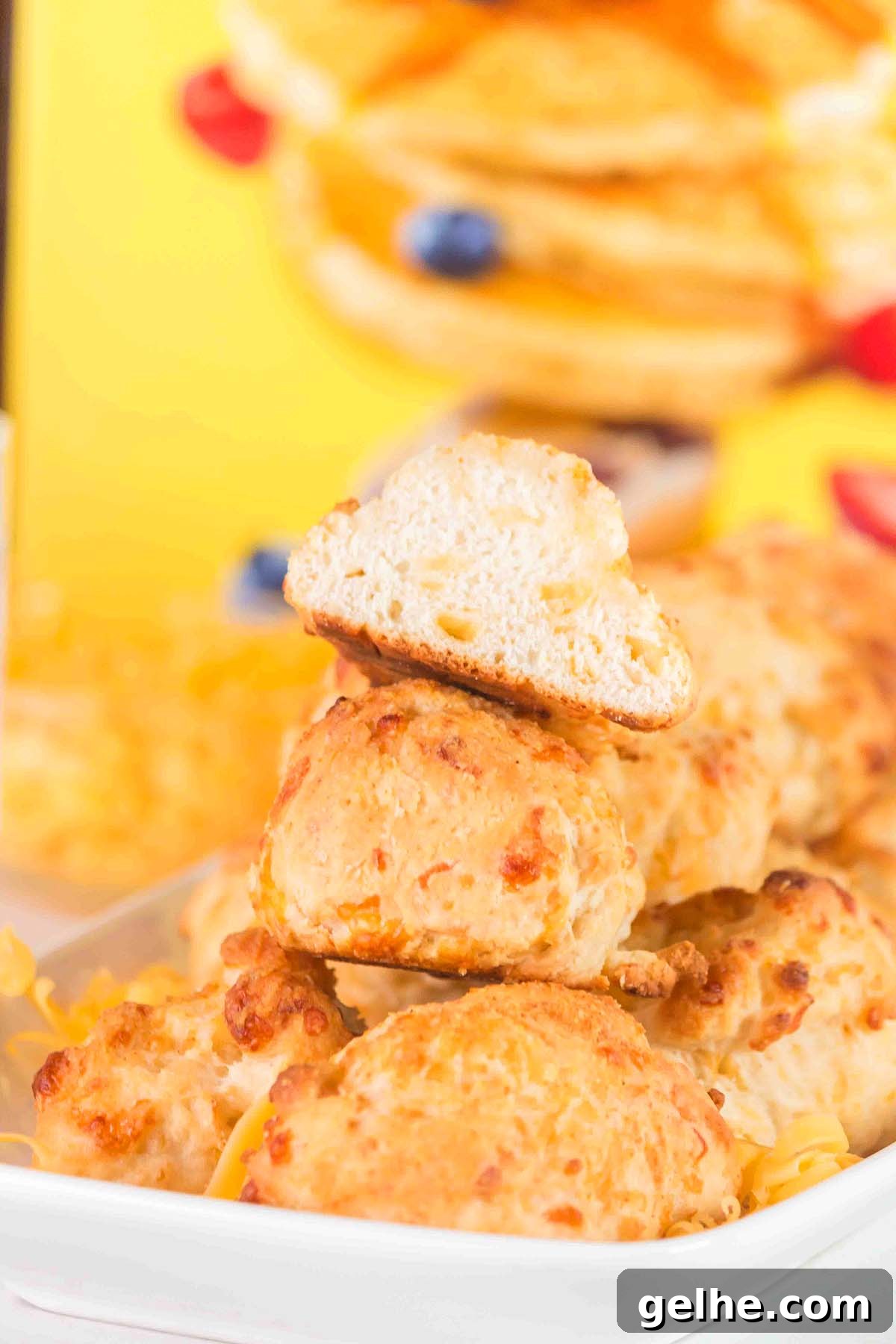 Flaky Cheddar Biscuits Made with Bisquick 4 A stack of golden-brown Bisquick cheddar biscuits with one biscuit halved on top, set against a rich yellow background.