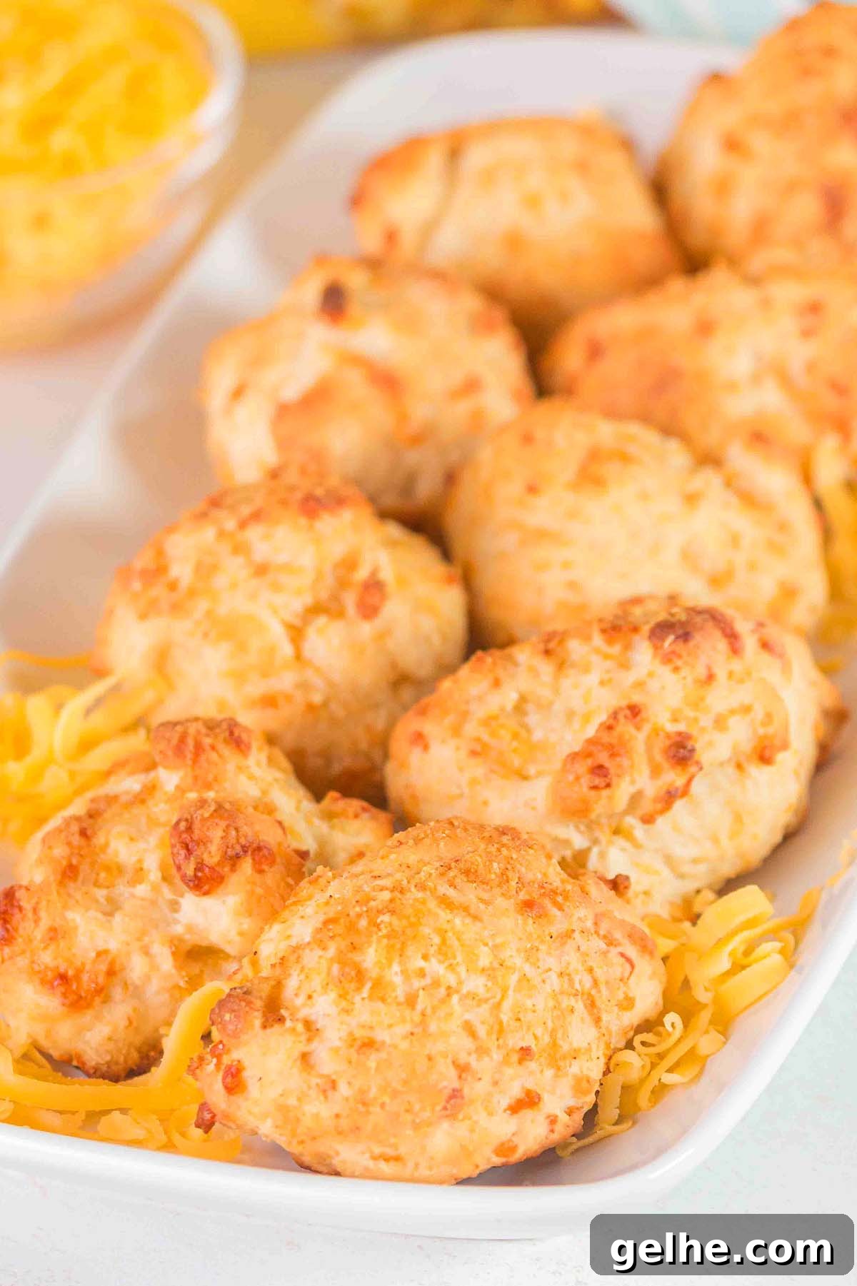 Flaky Cheddar Biscuits Made with Bisquick 5 A plate of six golden-brown Bisquick cheddar biscuits garnished with shredded cheese.