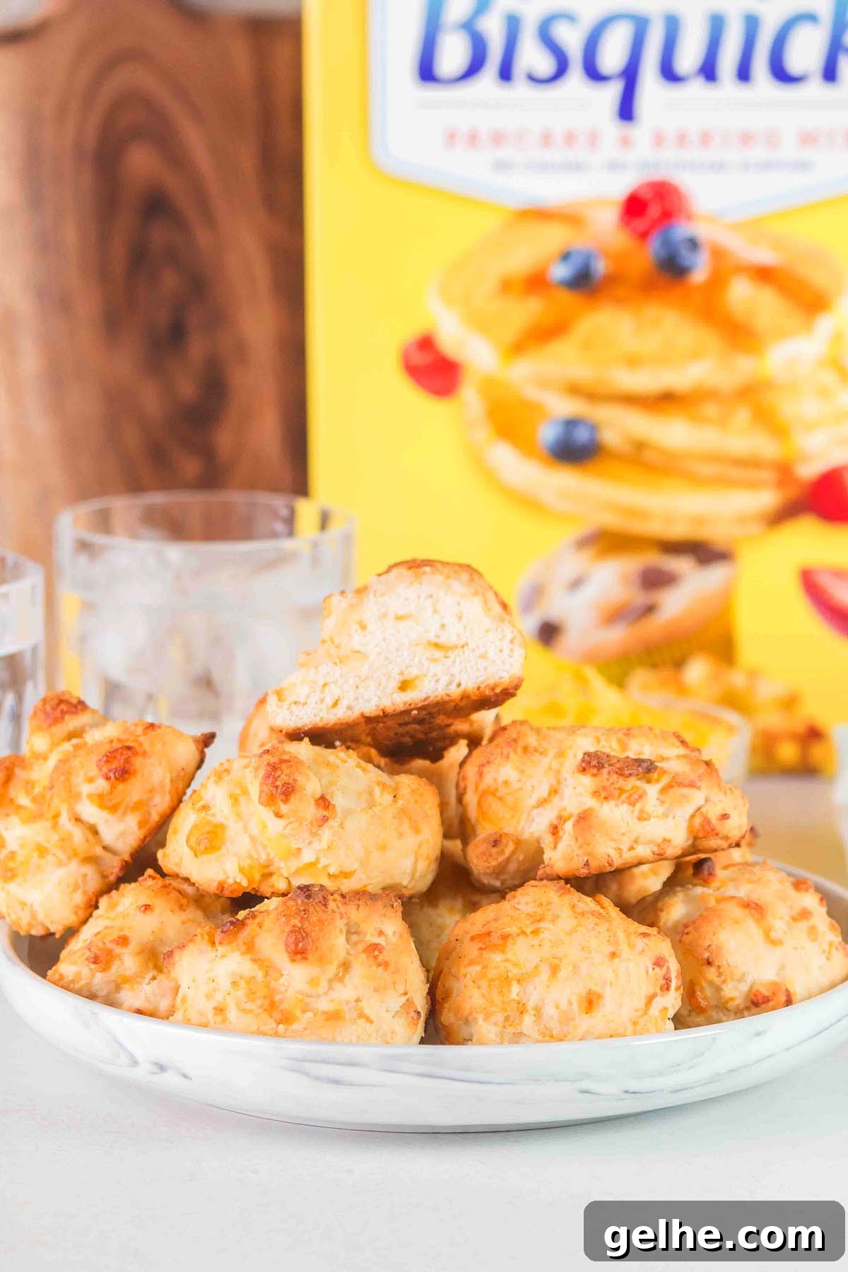 Flaky Cheddar Biscuits Made with Bisquick 7 A plate of delectable Bisquick cheddar bay biscuits is showcased in front of a Bisquick box, with two glasses of water subtly complementing the scene in the background.